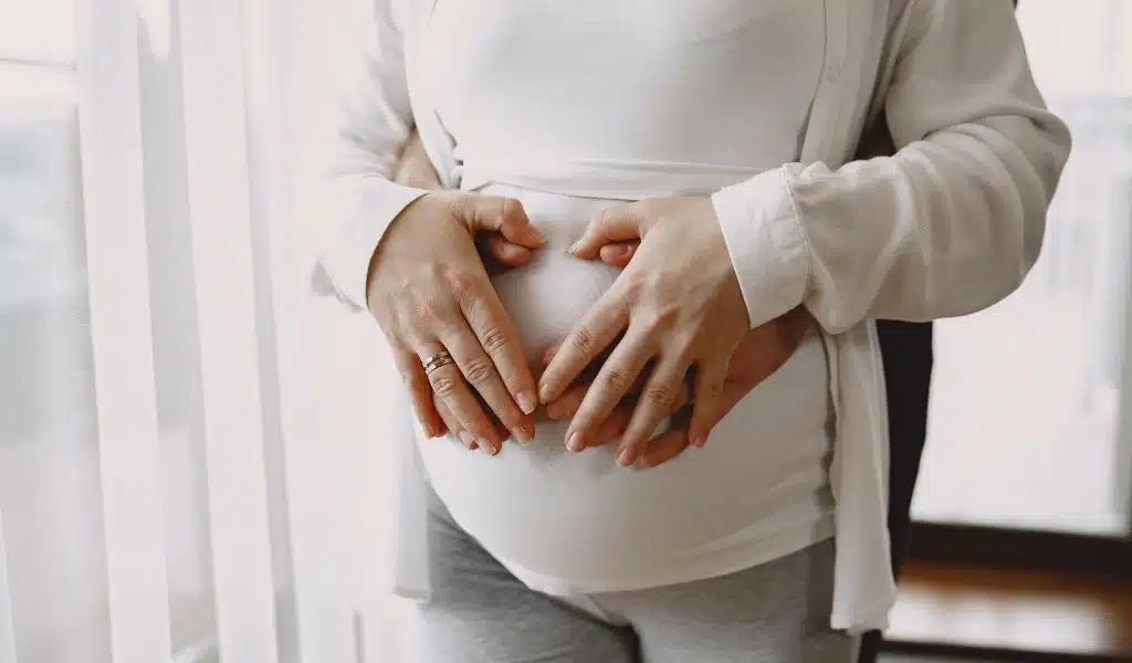 Mains d'un couple homme femme posées sur le ventre de la femme enceinte habillée en blanc