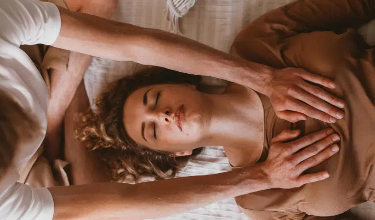 Mains posées sur les épaules d'une femme allongée pendant une séance de toucher