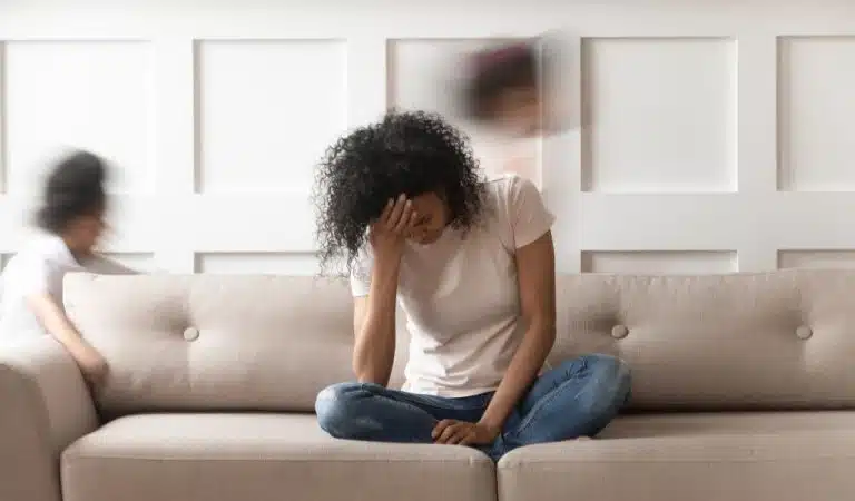 Femme assise sur un canapé, la tête dans la main, entourée d'enfants agités